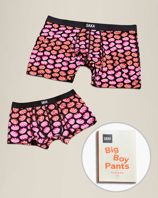 Two pairs of SAXX Father/Son boxer briefs with a candy pattern displayed on a beige background with a circular inset showing a box with 'Big Boy Pants'