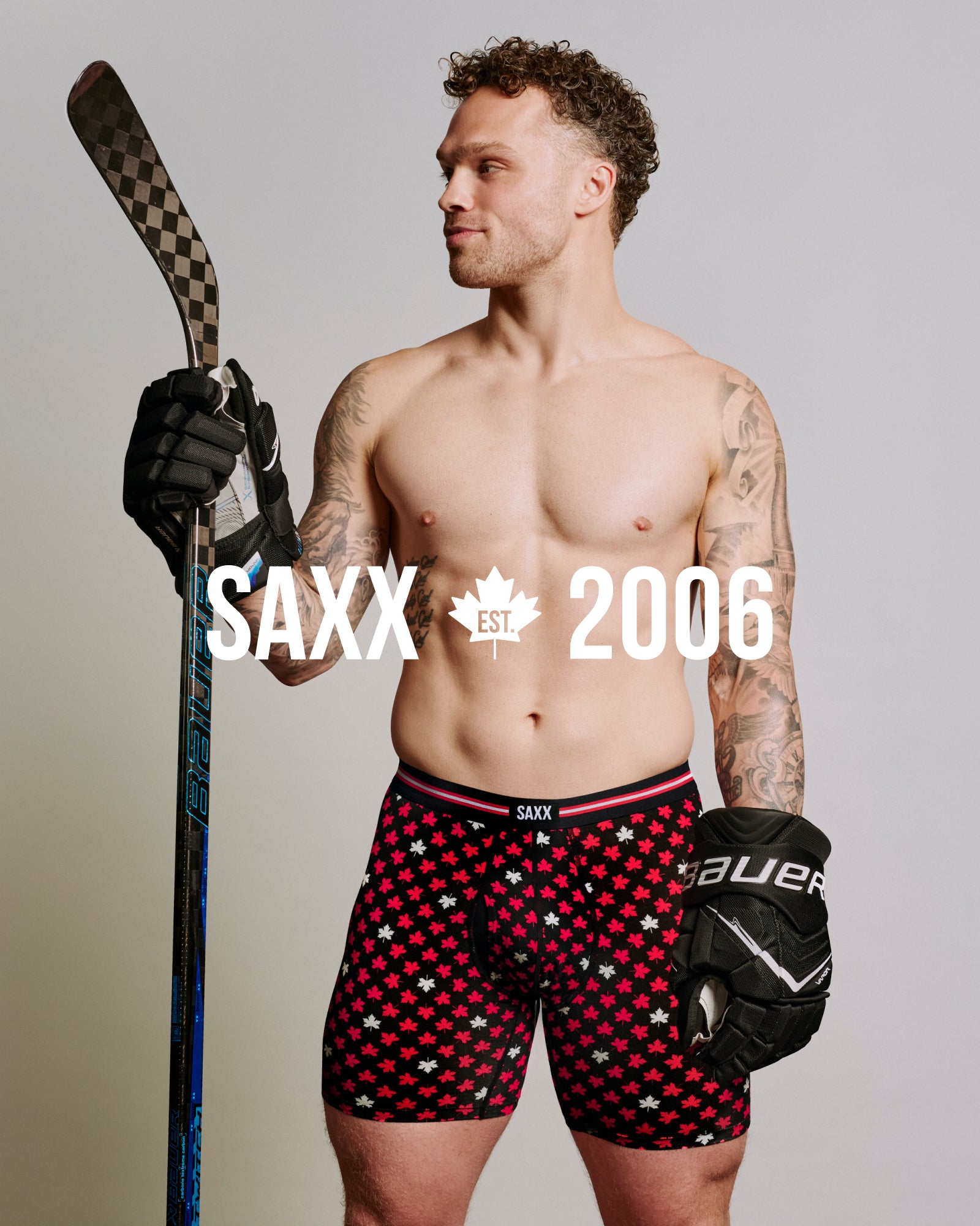 Max Domi wearing Canadian flag print Vibe Xtra boxer brief underwear and hockey gloves while holding a hockey stick with SAXX est. 2006 text