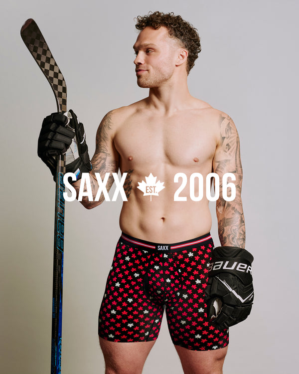 Max Domi wearing Canadian flag print Vibe Xtra boxer brief underwear and hockey gloves while holding a hockey stick with SAXX est. 2006 text