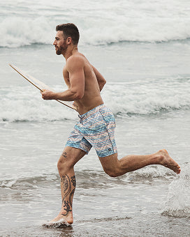 Man running on a beach wearing patterned swim shorts.