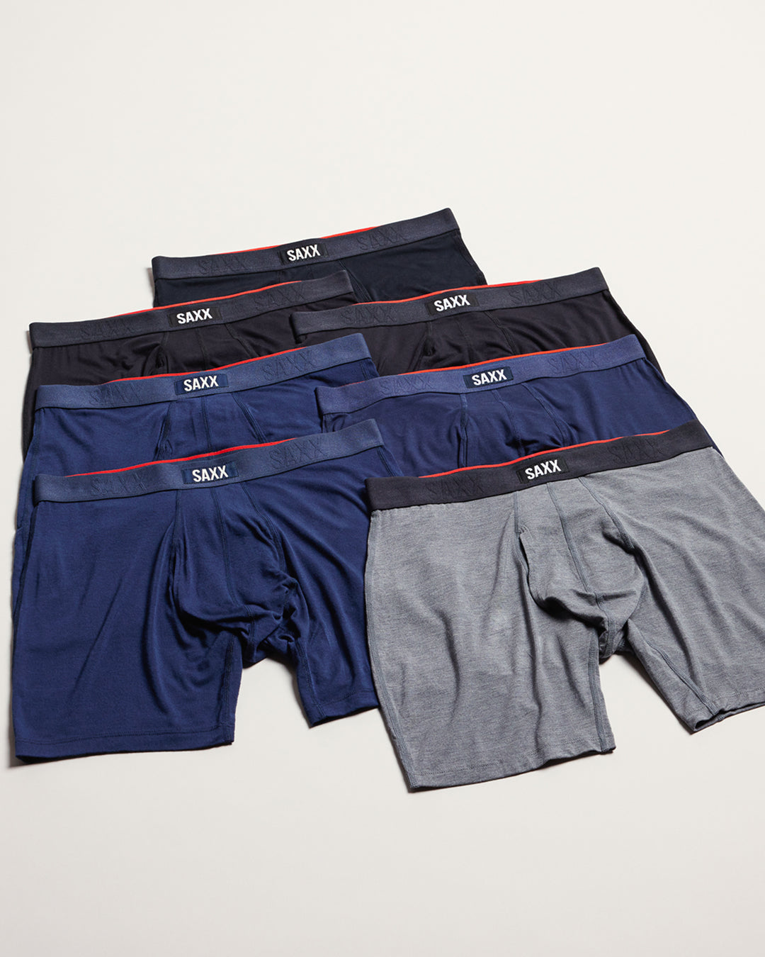 A set of five SAXX men's boxer briefs in various colors, including navy, charcoal, black, and heather gray, arranged in a fan-like stack on a light beige background.