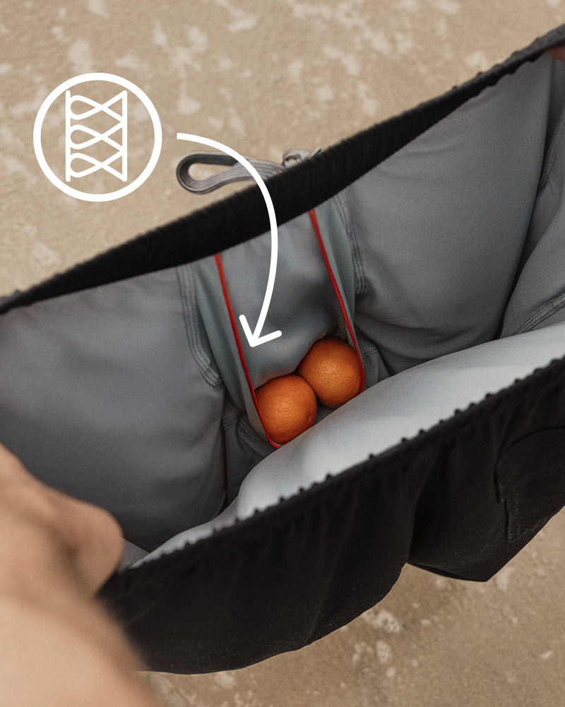 Close-up of a gray and black bag interior with a zipper pocket holding two orange fruit, plus a white overlay arrow and icon pointing to the pocket.