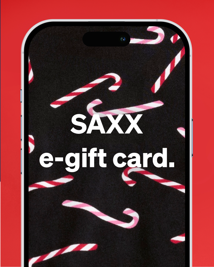 A smartphone centered on a bright red background, displaying a black screen with white text reading 'SAXX e-gift card.' and red-and-white candy cane illustrations.