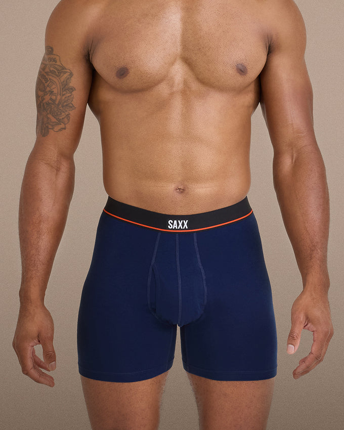 A man wearing navy blue boxer briefs with a black waistband, orange accent line, and the brand name 'SAXX' in white on the front.
