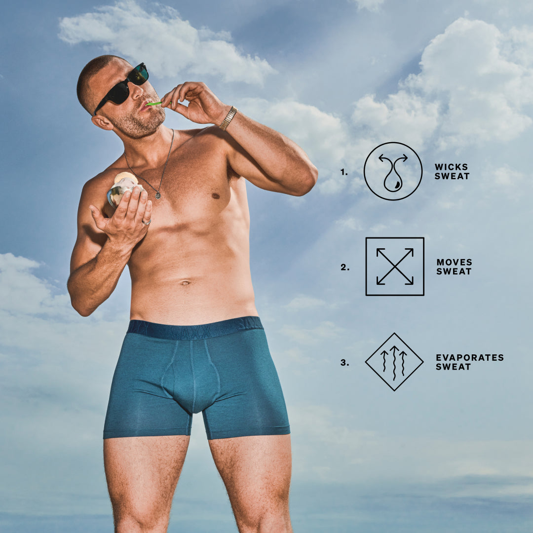 Man wearing blue SAXX Boxer Briefs standing in front of blue sky. Icons reading: wicks sweat, moves sweat, evaporates sweat.