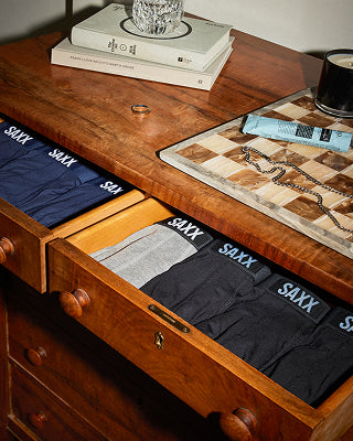 Three pairs of blue boxer briefs laid on top of each other on a wood sideboard. 