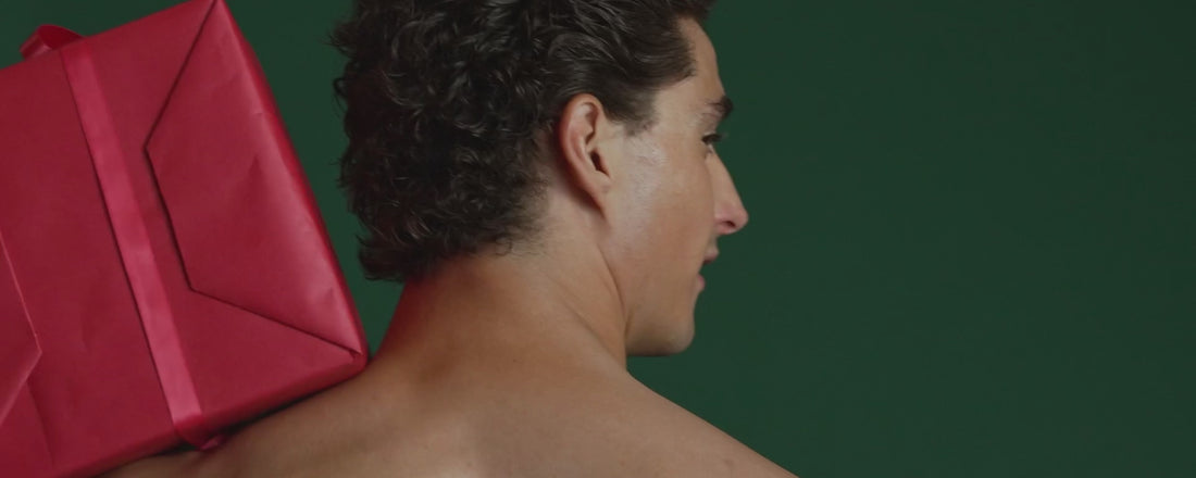 A person wearing a santa hat and SAXX underwear in various holiday prints, stacking presents