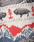Close-up of a knitted fabric with red trees, gray bison, and blue mountains.
