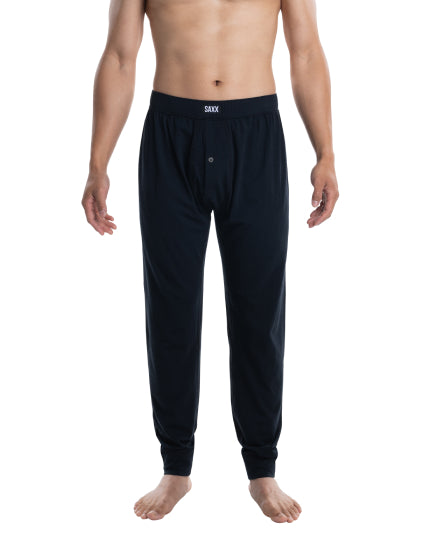 Shirtless man in black sleep pants standing in front of white background